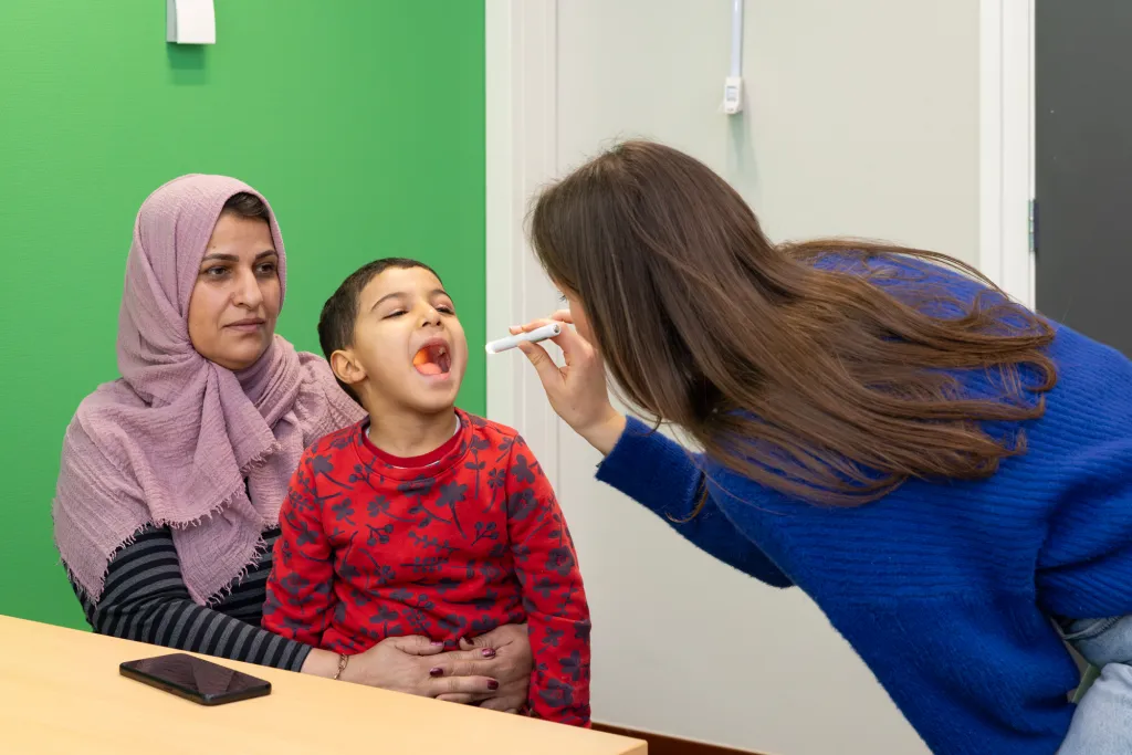 Praktijkverpleegkundige onderzoekt kind die bij moeder op schoot zit